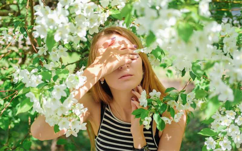 Chica joven rodeada de flores se tapa los ojos con una mano