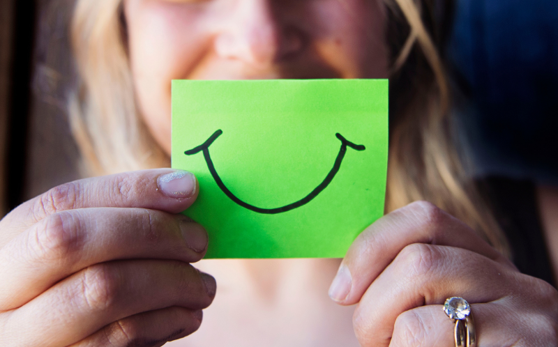 Chica sujetando un post-it con cara sonriente dibujada