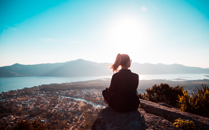 Chica sentada en la cima de una montaña mirando al horizonte soleado